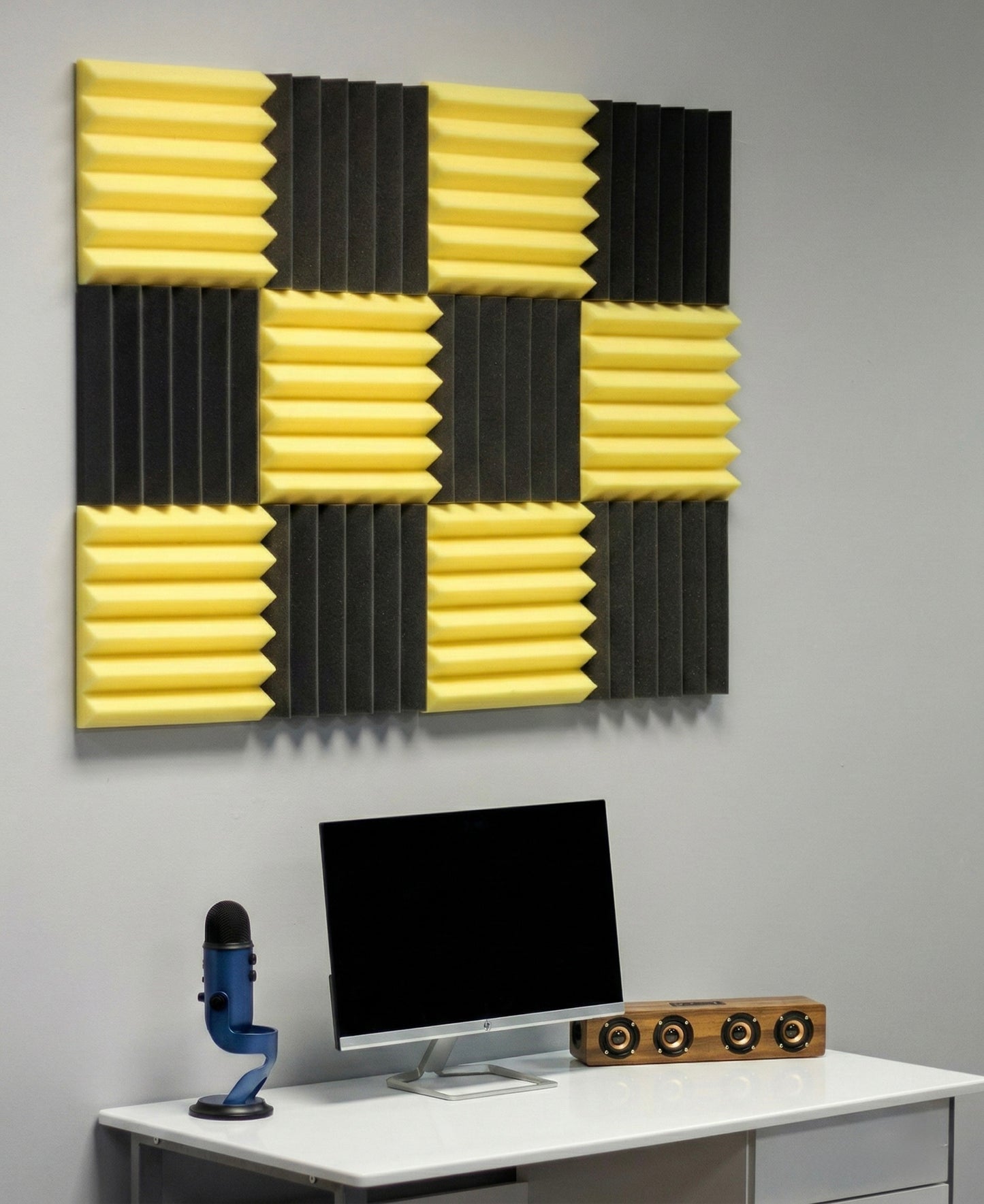 Acoustic foam panels on a gray wall above a desk with a computer setup.